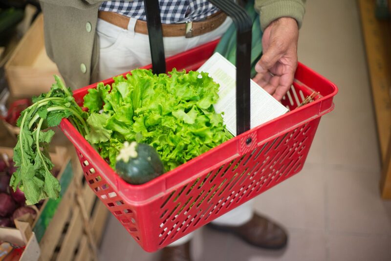 Friss zöldségekkel teli piros bevásárlókosár az üzletben